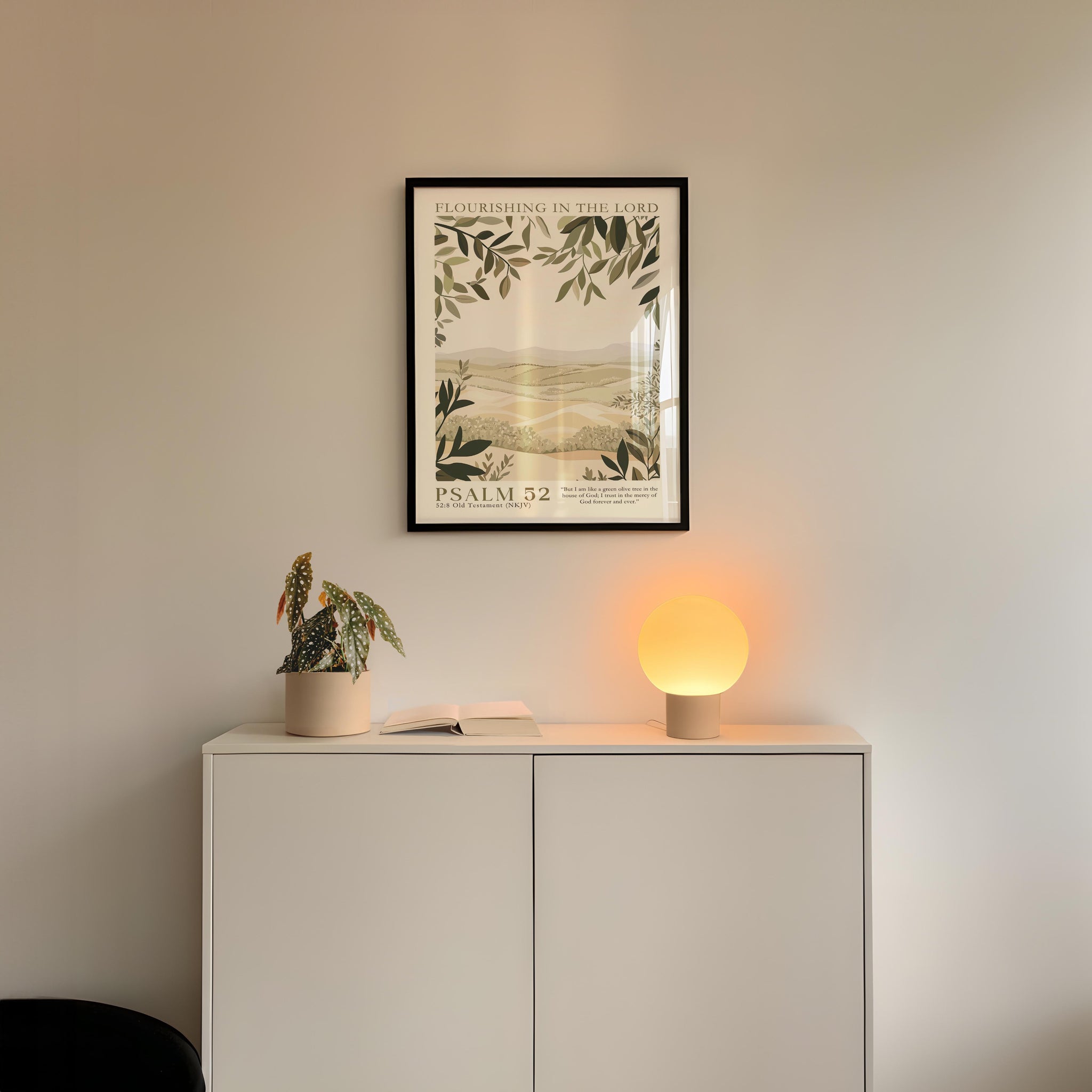 a white cabinet with a plant and a lamp on top, and a framed poster of a landscape hanging on the wall above it.