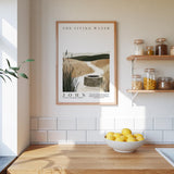 a kitchen scene with a framed poster of a well and a bowl of lemons on a wooden countertop.