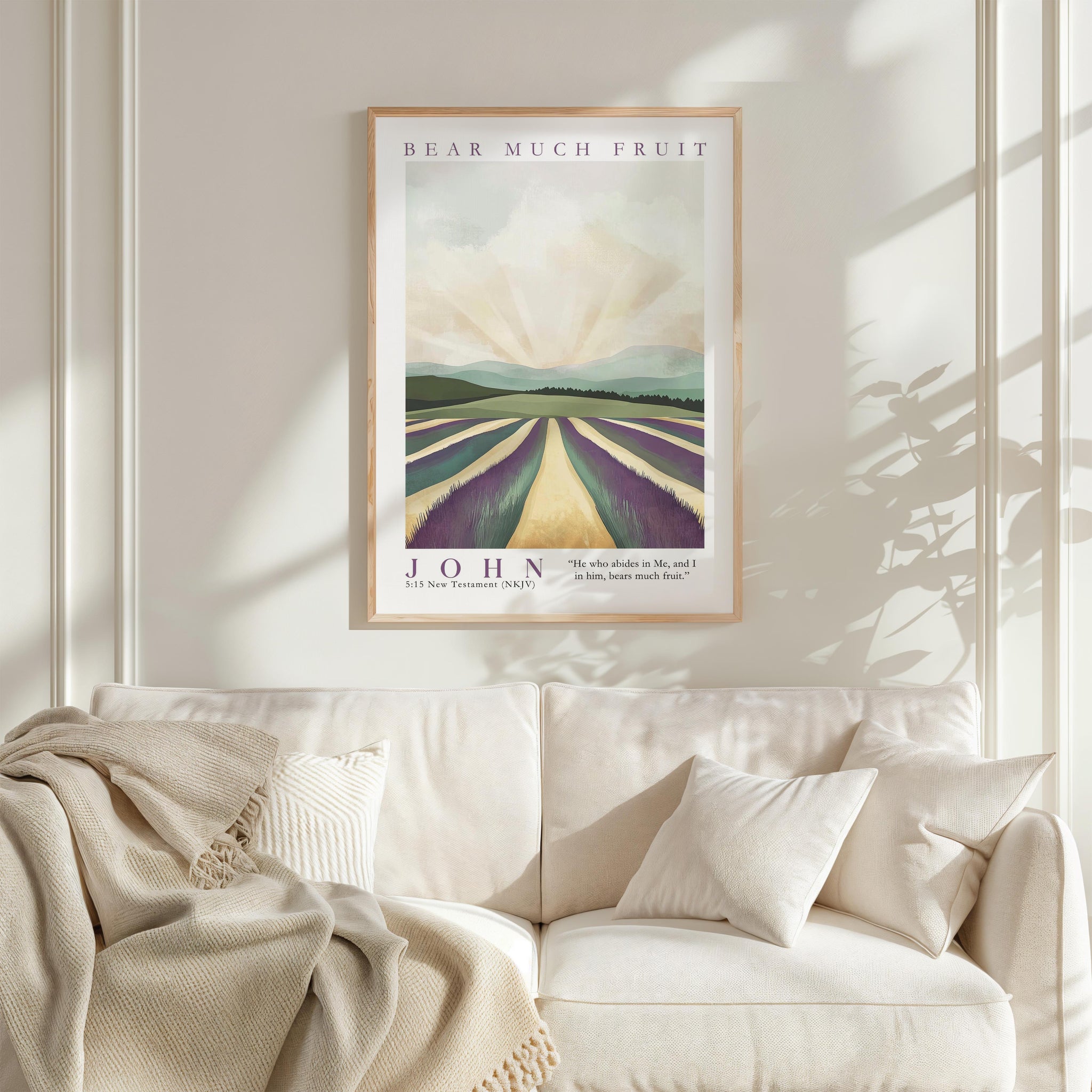 a framed poster of a landscape with a field of fruit trees, hanging on a wall above a white couch with a blanket draped over it.