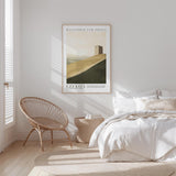 a serene bedroom scene with a bed, a woven chair, and a framed poster of a desert landscape hanging on the wall.