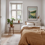 A cozy bedroom with a large bed, a nightstand with a potted plant, and a framed poster on the wall.