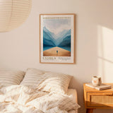 a bedroom scene with a framed poster of a person walking through a mountainous landscape hanging on the wall above a bed with striped bedding.