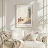 a framed poster of a desert scene with a white sofa and a plant in the foreground.