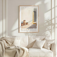 a framed poster of a desert scene with a white sofa and a plant in the foreground.