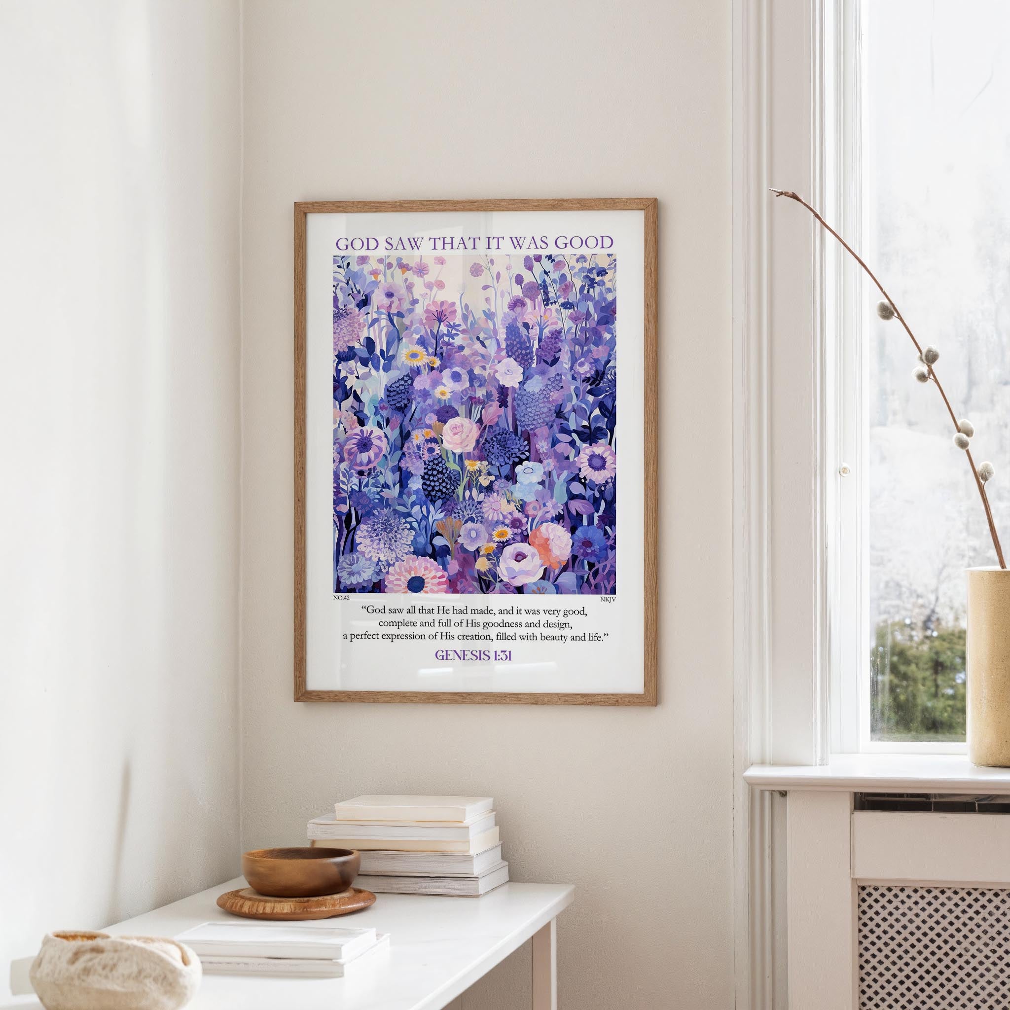 a framed poster of a vibrant purple and blue floral pattern hanging on a white wall. Below the poster, there is a small table with a stack of books and a wooden bowl.