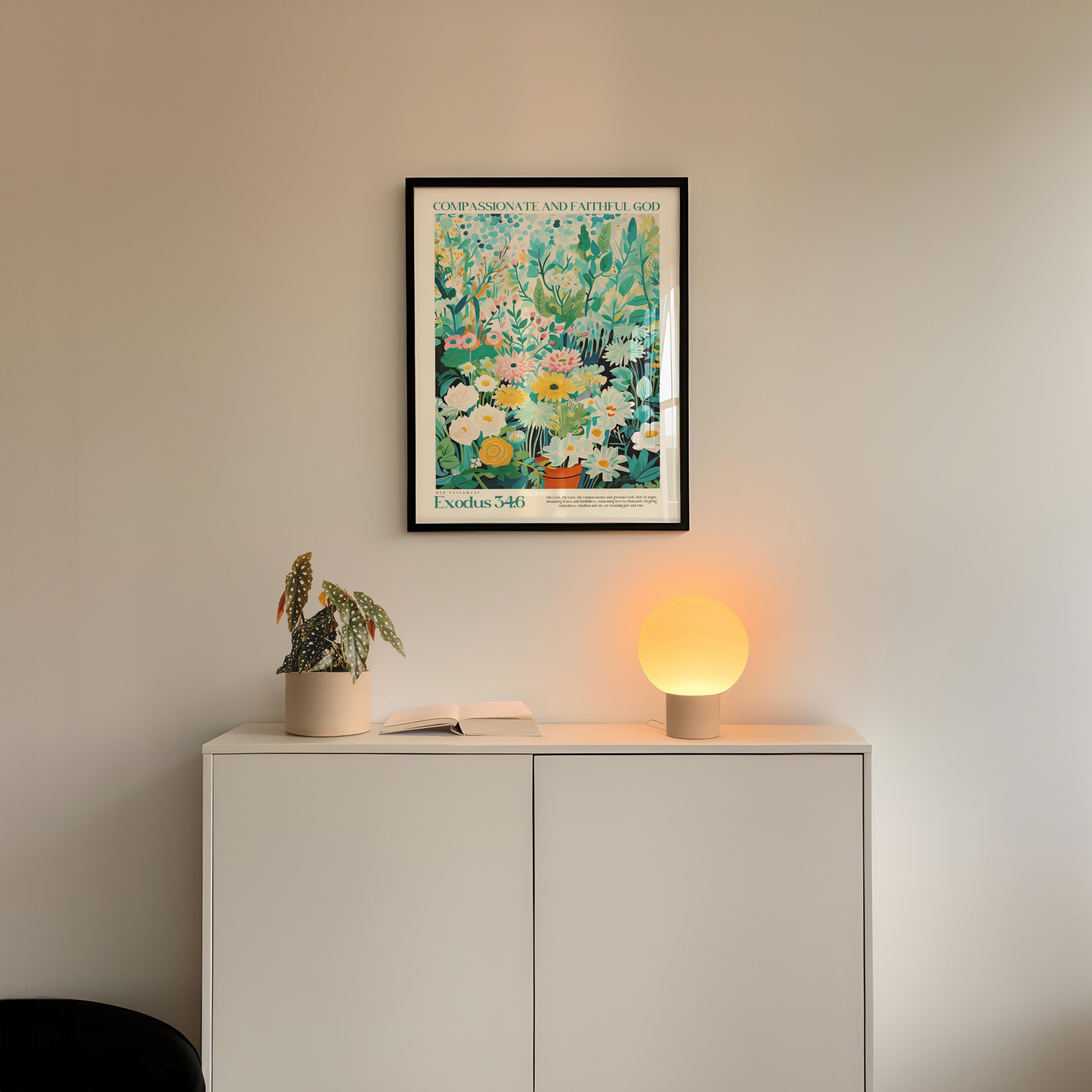 a white cabinet with a plant and a lamp on top, and a framed poster of a colorful floral design hanging on the wall above the cabinet.