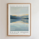 The image is a framed poster with a serene landscape depicting a calm body of water surrounded by mountains. The text "BESIDE THE STILL WATERS" is written at the top of the poster, and the phrase "PSALM" is written at the bottom. The poster also includes a Bible verse from the Old Testament (NIV) that reads, "He makes us to lie down in green pastures, leads us beside the still waters."
