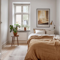 A cozy bedroom with a large bed, a nightstand with a plant, and a framed poster on the wall.