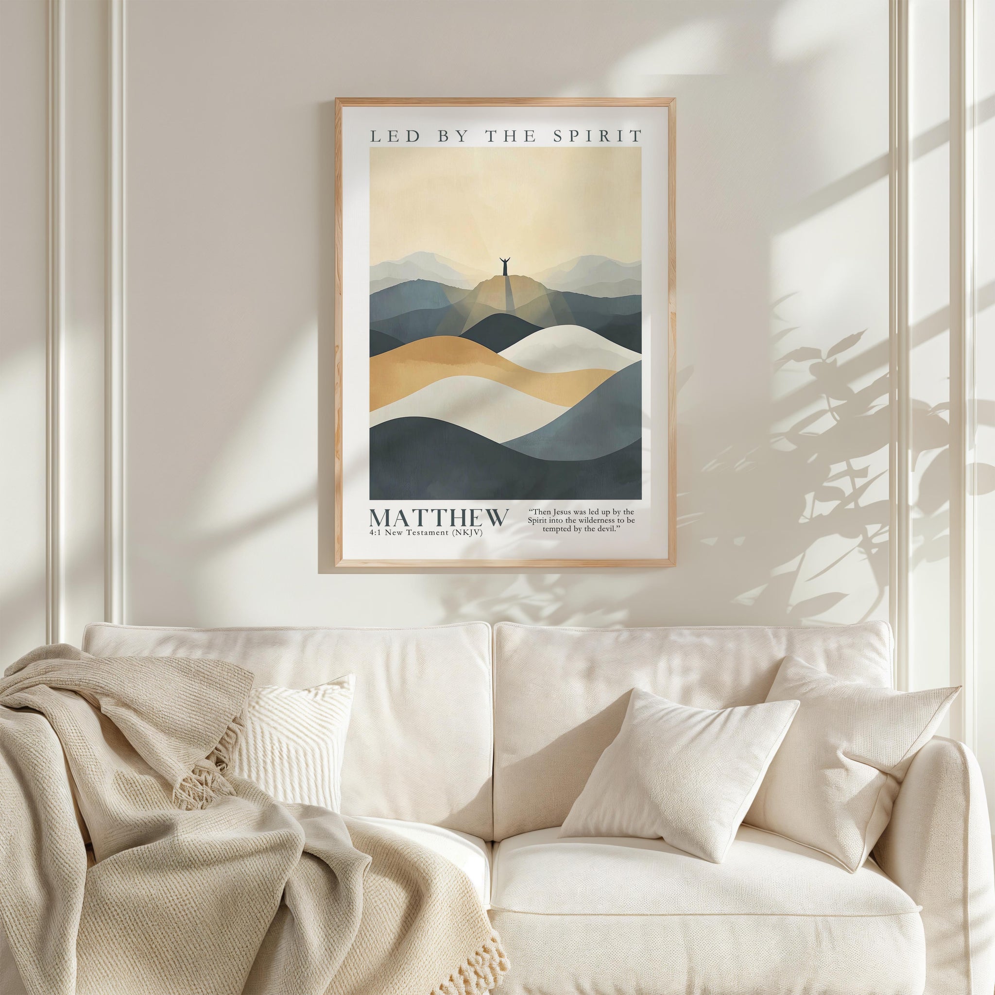 a framed poster of a mountain landscape with a person standing on top, hanging on a wall above a white couch with a blanket draped over it.