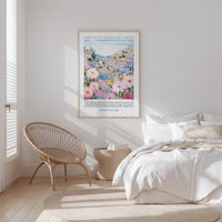 a bedroom with a bed, a wicker chair, and a framed poster of a colorful floral landscape hanging on the wall.