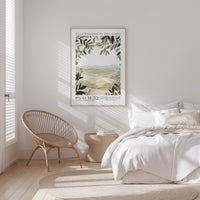 A bedroom with a bed, a woven chair, and a framed poster of a landscape on the wall.