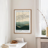 a framed poster of a flock of birds flying over a mountainous landscape, hanging on a wall in a room with a white table and a window.