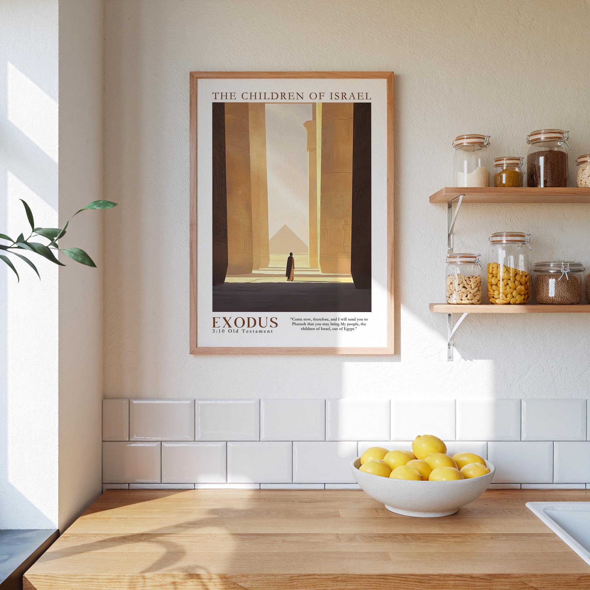 a framed poster of a man standing in front of a temple, with the text "Exodus 3:10 Old Testament" below it. The poster is hanging on a wall above a wooden counter with a bowl of lemons on it. The counter also has various jars and bottles on it, and there is a plant in the corner of the room.