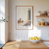 a kitchen scene with a framed poster of a desert landscape hanging on the wall above a wooden countertop with a bowl of lemons.