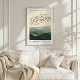 a framed poster of a flock of birds flying over a mountainous landscape, hanging on a wall above a white couch with a blanket draped over it.