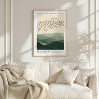a framed poster of a flock of birds flying over a mountainous landscape, hanging on a wall above a white couch with a blanket draped over it.
