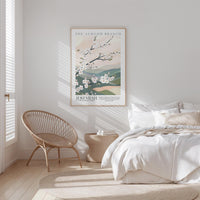 a serene bedroom scene with a bed, a woven chair, and a framed poster of a blooming tree on the wall.