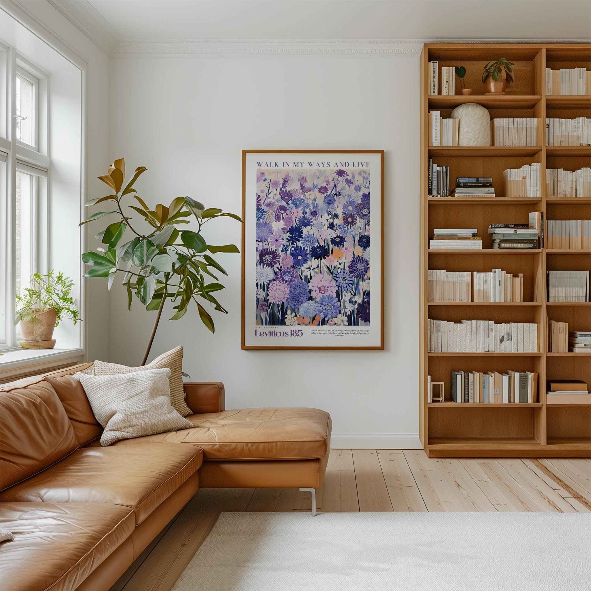 a cozy living room with a brown leather sofa, a large window, a bookshelf filled with books, and a framed poster of purple flowers on the wall.