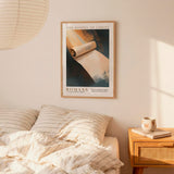 a bedroom setting with a framed poster of a roll of toilet paper hanging on the wall above a bed with striped bedding.