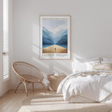 a serene bedroom scene with a large bed, a woven chair, and a framed poster of a mountain landscape hanging on the wall.
