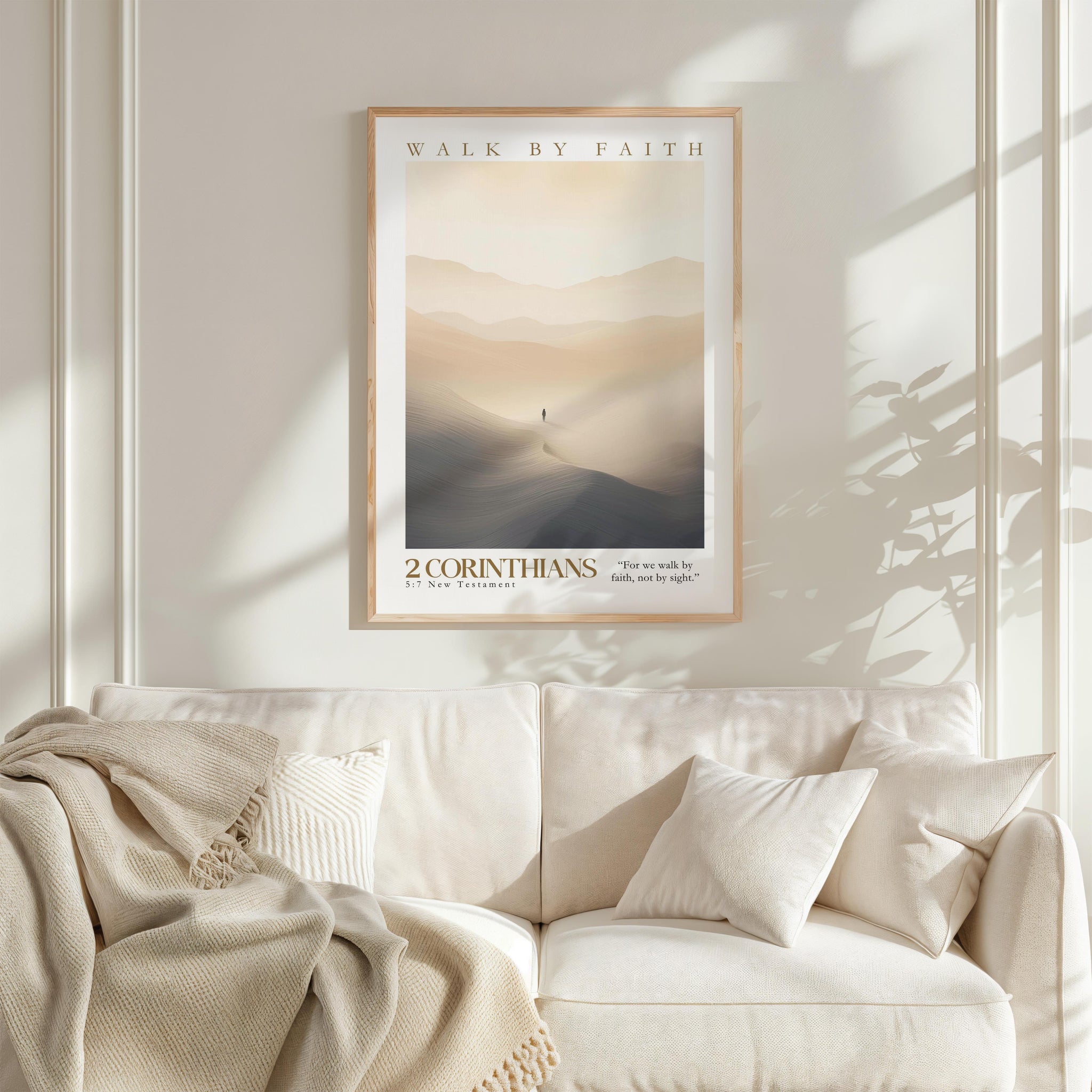 a framed poster of a person walking on a path in a desert landscape, with mountains in the background. The poster is hung on a wall above a white couch with pillows.