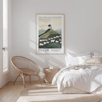 A bedroom with a bed, a woven chair, and a framed poster of a pastoral scene with sheep on a hill.