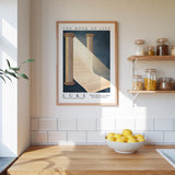 a framed poster of a staircase leading up to a white curtain, hanging on a wall above a wooden counter with a bowl of lemons.