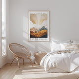 A bedroom with a bed, a woven chair, and a framed poster of a mountain landscape on the wall.