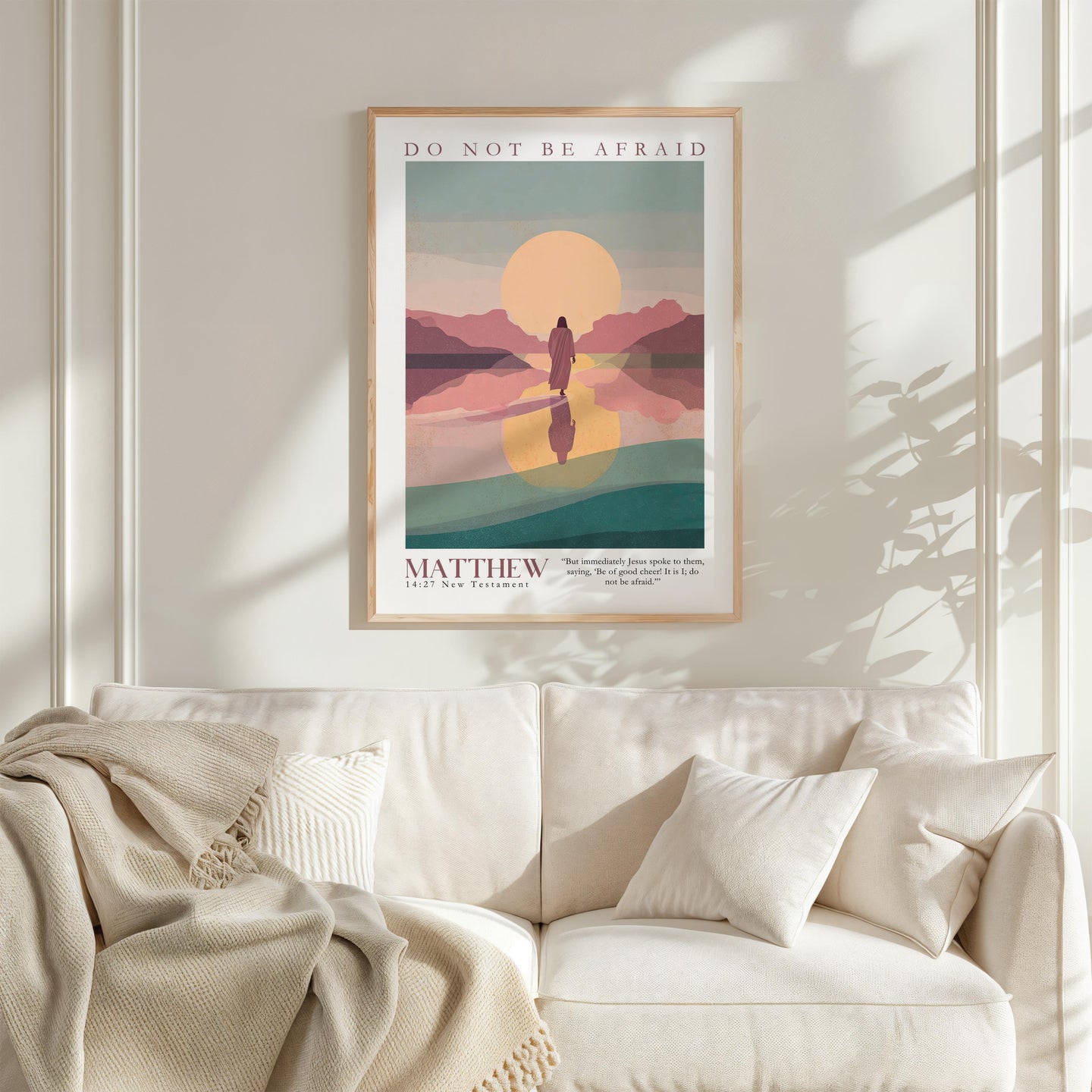 a poster of a person walking on a path with mountains in the background, hanging on a wall above a white couch.