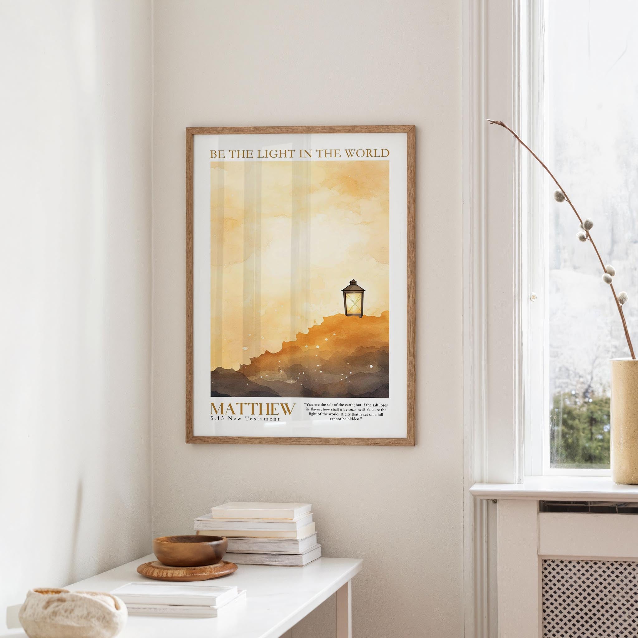 a framed poster of a serene landscape with a lantern on a hill, hanging on a wall in a room with a window and a small table with books and a bowl.