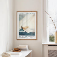a framed poster of a blue and white abstract design hanging on a wall, with a white table below it holding a stack of books and a small vase.