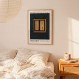 a bedroom with a framed poster of a window and a candle on the wall above a bed with striped bedding. There is also a wooden nightstand with a coffee mug and a book on it.
