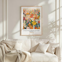 a poster of a vibrant floral arrangement hanging on a wall above a white couch with a blanket draped over it.
