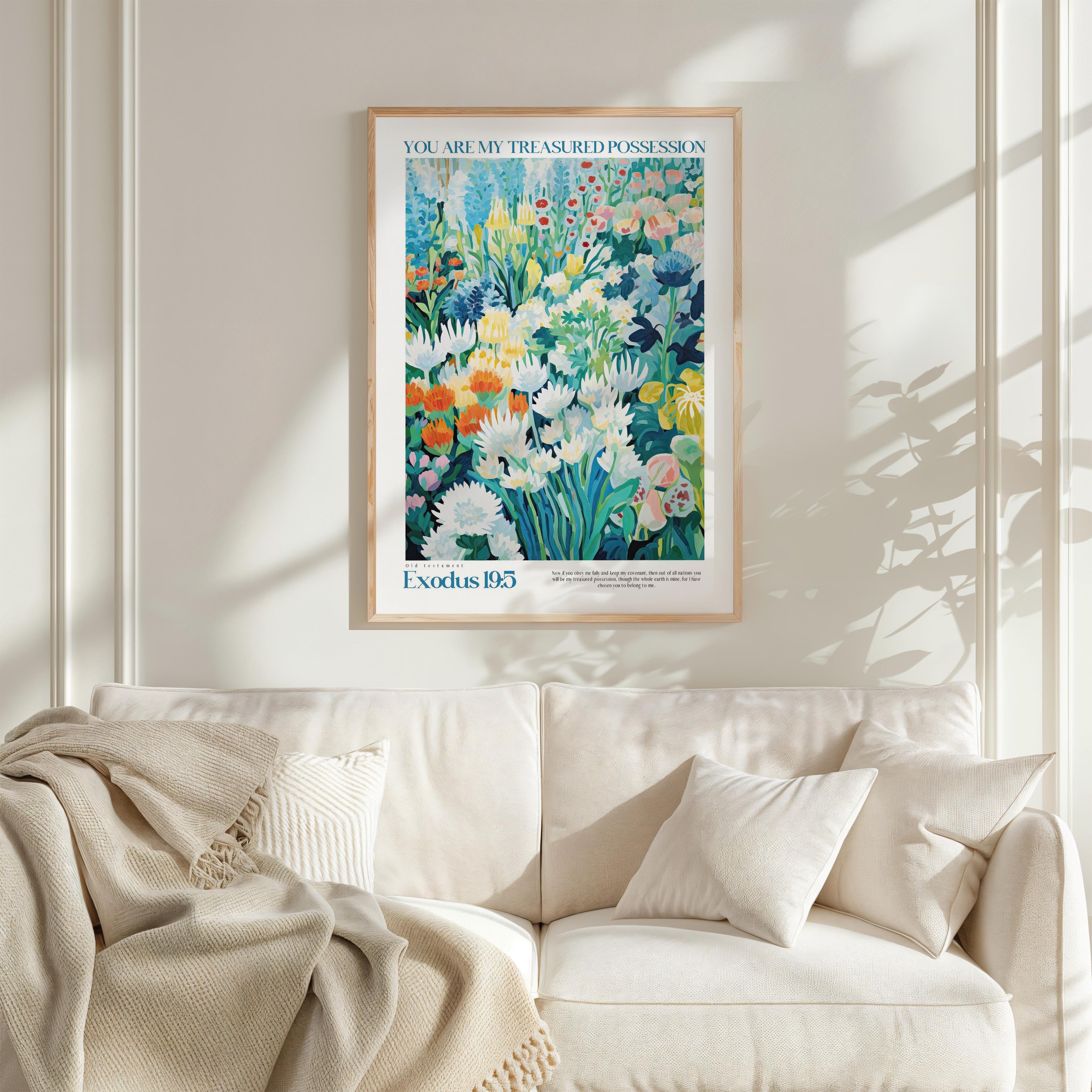 a framed poster of a colorful garden scene hanging on a wall above a white couch with a blanket draped over it.