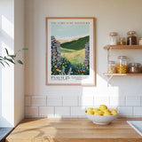a kitchen scene with a framed poster of a countryside landscape hanging on the wall above a wooden countertop with a bowl of lemons.