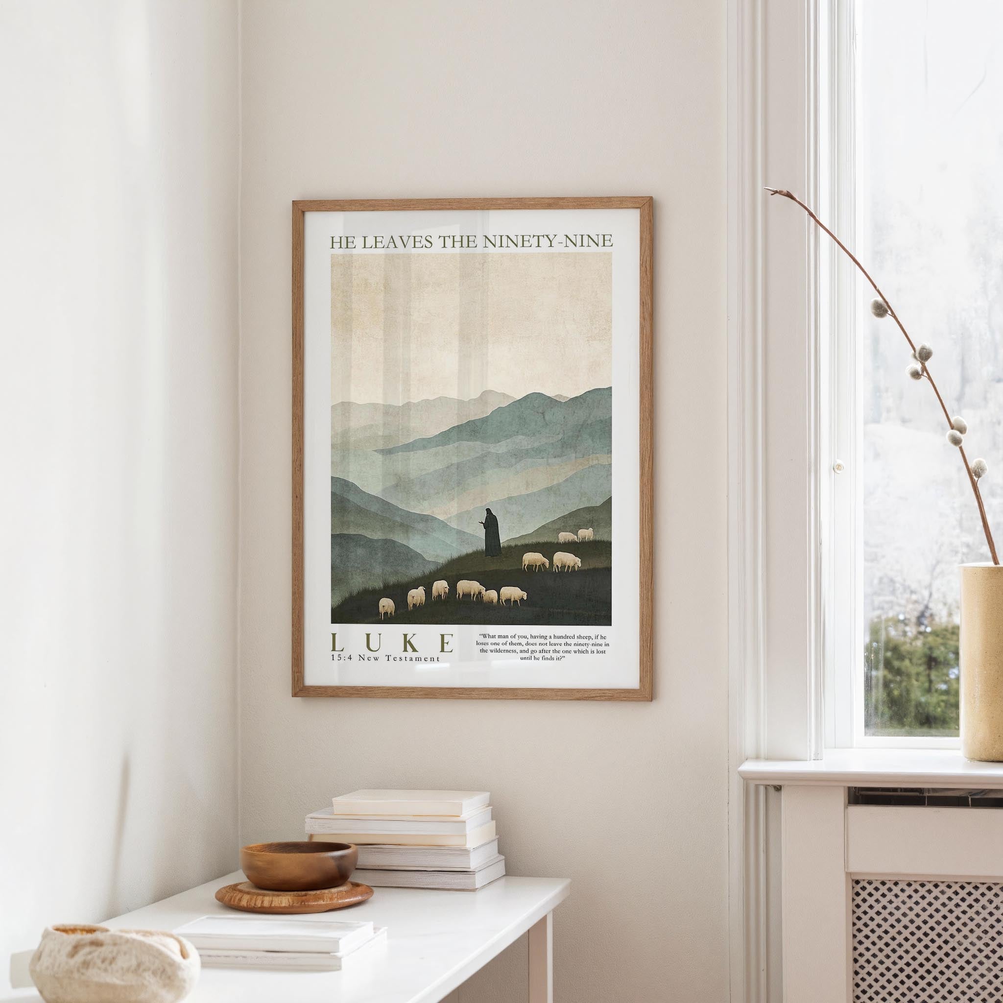 a framed poster of a pastoral scene with a shepherd tending to his flock, hanging on a wall in a room with a window and a small table with books and a bowl.
