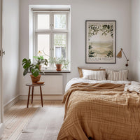 A cozy bedroom with a large bed, a nightstand with a potted plant, and a framed poster on the wall.