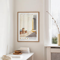 a framed poster of a room with a window, a table with books and a bowl, and a plant on a shelf.