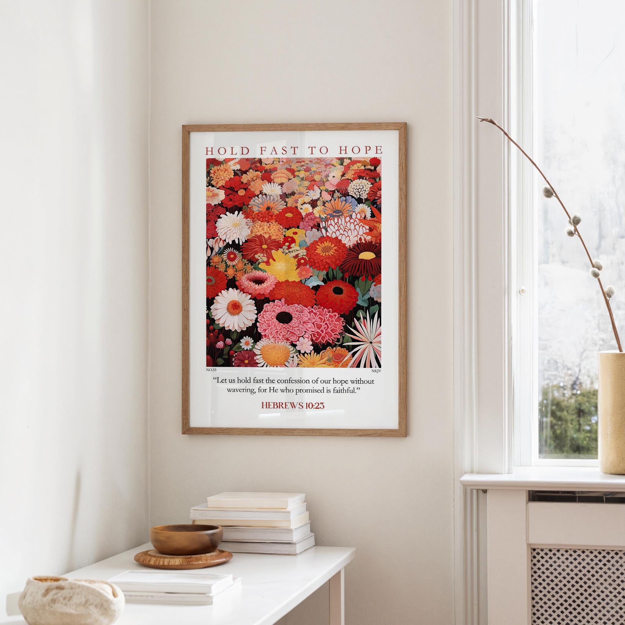 a framed poster of a vibrant floral arrangement hanging on a wall, with a stack of books and a small vase on a white table below it.