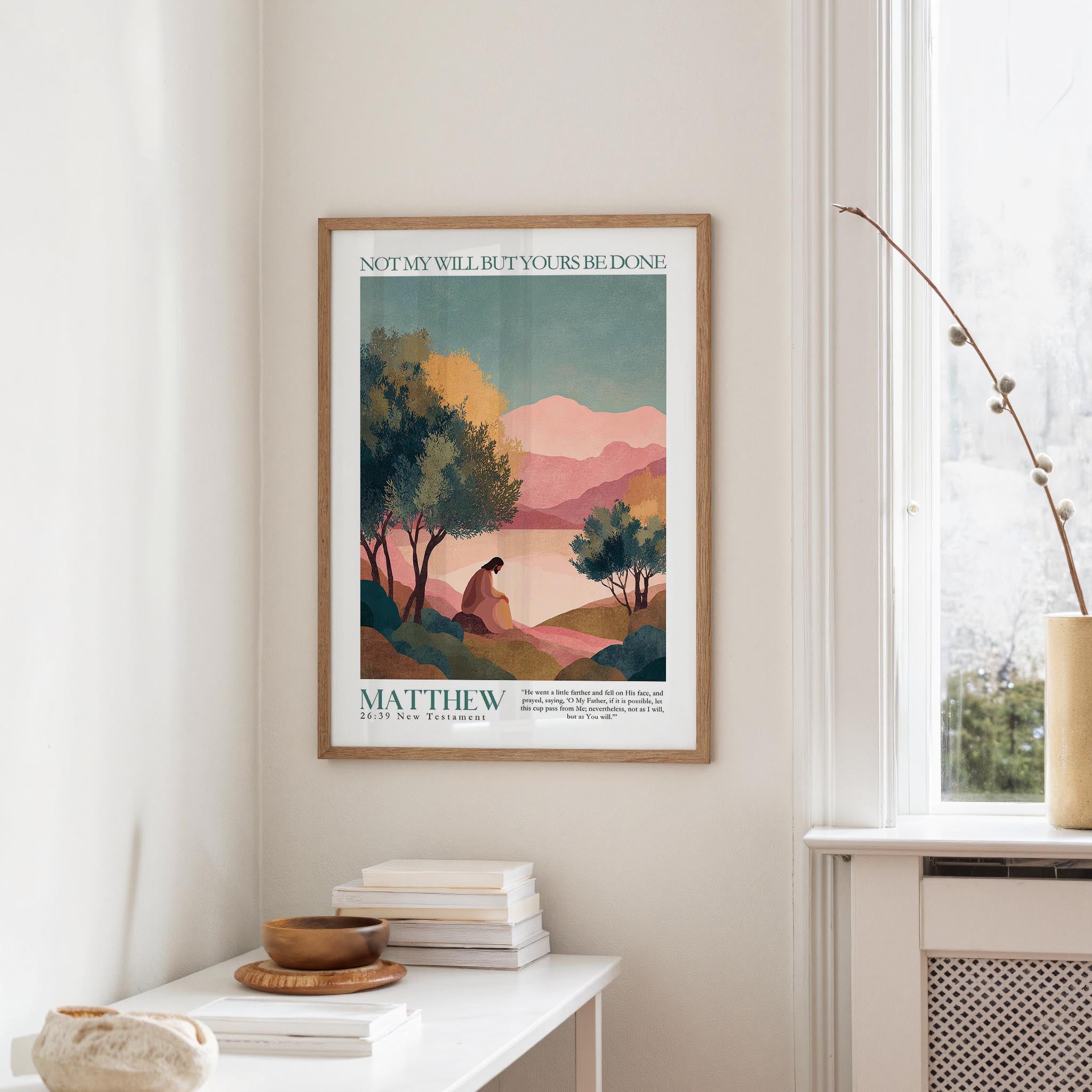 a framed poster of a landscape with mountains and trees, hanging on a wall above a white table with a stack of books and a small vase.