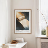 a framed poster of a book titled "The Gospel of Christ" hanging on a wall, with a white table and a vase of flowers in the foreground.