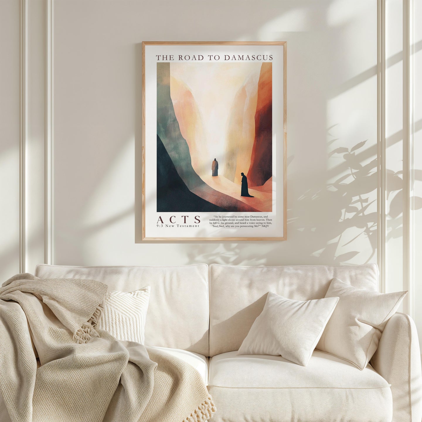 a framed poster of a desert landscape with two figures walking through it, hanging on a wall above a white couch with a blanket draped over it.