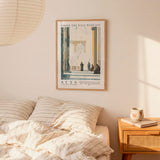 a bedroom scene with a framed poster of a classical architectural structure hanging on the wall above a bed with striped bedding.