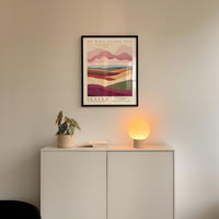 a minimalist interior design with a framed poster of a landscape, a potted plant, and a small lamp on a white cabinet.