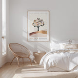 a serene bedroom scene with a bed, a woven chair, and a framed poster of a tree on the wall.