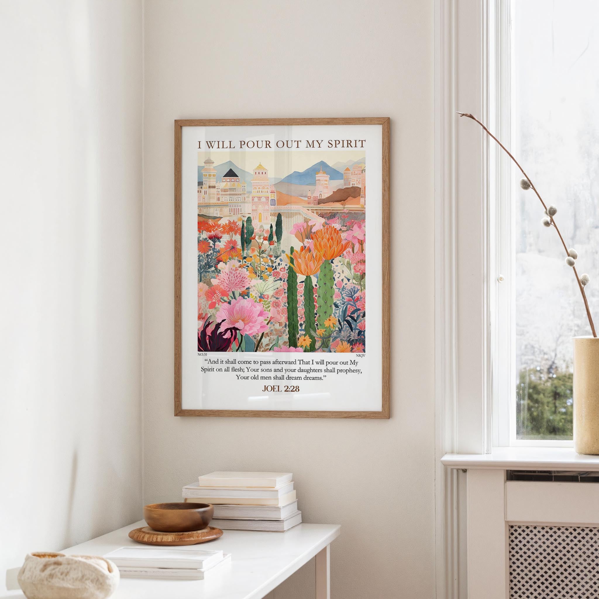 a framed poster of a colorful garden scene hanging on a wall, with a window and a small table with books and a vase nearby.