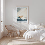 a serene bedroom scene with a bed, a woven chair, and a framed poster on the wall.