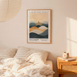 a bedroom setting with a framed poster of a mountain landscape hanging on the wall above a bed with striped bedding.