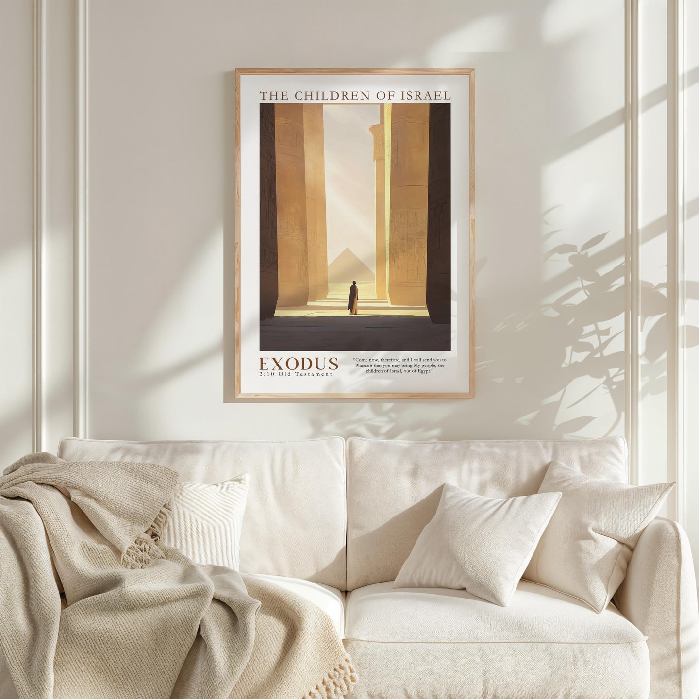 a framed poster of a desert landscape with a person walking through it, hanging on a white wall above a white couch with a blanket draped over it.