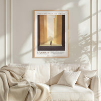 a framed poster of a desert landscape with a person walking through it, hanging on a white wall above a white couch with a blanket draped over it.